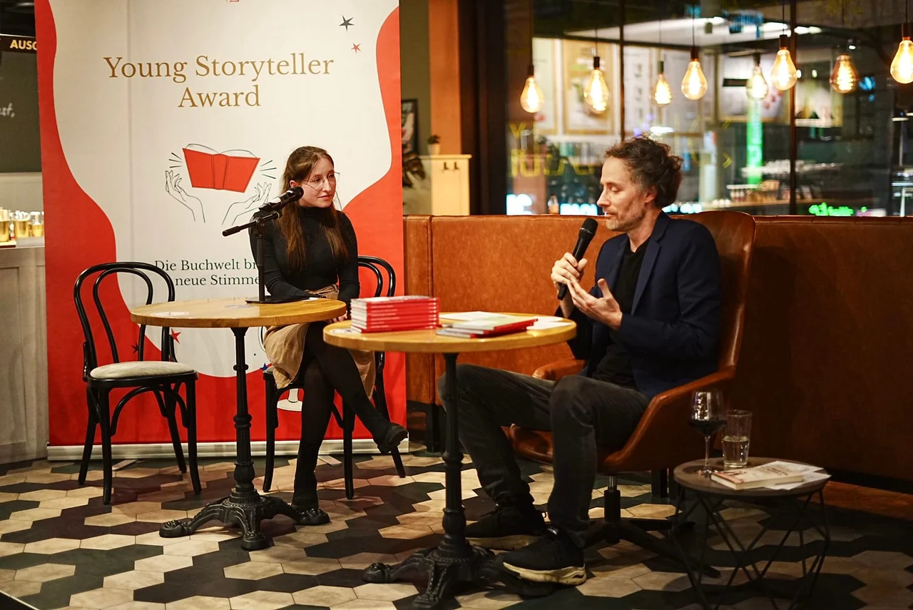 Gespräch auf einer Bühne vor einem Banner des Young Storyteller Awards.